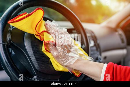 Young woman cleaning steering wheel in car with yellow wiper cloth, closeup detail to her hand Stock Photo