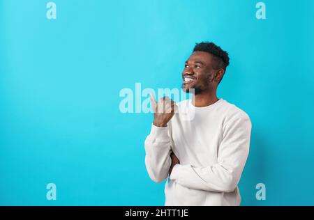 A surprised African student pointing his finger to the side at the copy space on a blue background Stock Photo