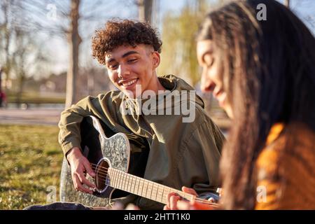 Young latin couple sitting at tree playing ukulele and guitar singing a song. happy feeling/relaxing concept Stock Photo