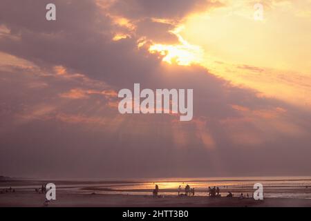Sunbeams over Cabourg, Normandy coast,.Sunset over the Atlantic Ocean. Sun behind dark clouds. Silhouettes of people on beach. Cote Fleurie, France Stock Photo