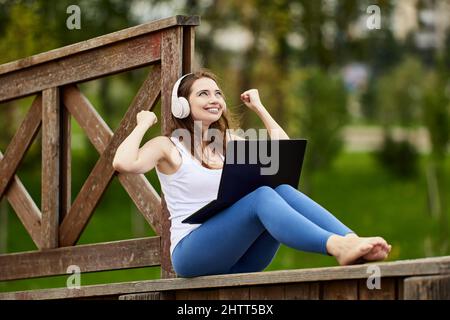 Good news for woman who makes remote work by laptop outdoors. Stock Photo
