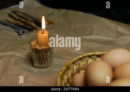 Candle with light. Rustic background. Tools for decorating Paschal eggs, Pysankas. Collection of eggs. Homemade pen for drawing eggs. Preparation for Stock Photo
