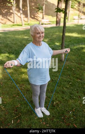 Happy senior woman in sportswear does excercise with jump rope in green park Stock Photo