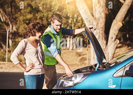 This is the problem right here. Shot of a young woman receiving roadside assistance from a young man after breaking down. Stock Photo