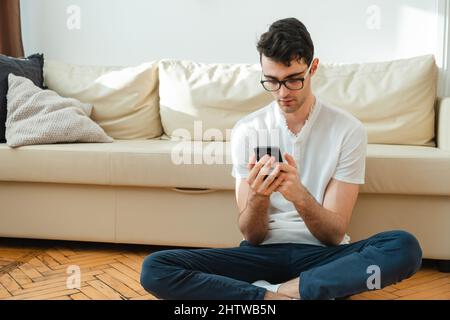 Portrait of a male freelancer who is always in touch at home. Handsome focused young man using his smartphone while sitting on the couch. Stock Photo