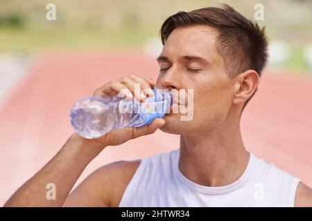 Getting some liquid refreshment. Shot of a handsome young athlete taking a drink from a water bottle. Stock Photo