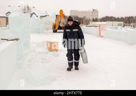 A working assembler in winter overalls with an iron trough walks along a construction site Stock Photo