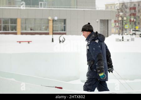 A working assembler in winter overalls with an iron trough walks along a construction site Stock Photo