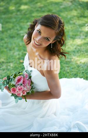 Beaming on her big day. A gorgeous bride sitting on grass. Stock Photo