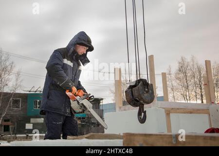 Worker with a chainsaw in hand at the assembly site Stock Photo