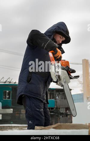 Worker with a chainsaw in hand at the assembly site Stock Photo