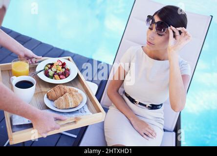 Relaxing while on holiday. A posh young woman looking dubiously at the food brought to her. Stock Photo