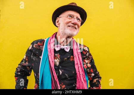 Happy senior man looking away thoughtfully while standing against a colourful background. Pensive elderly man reflecting on happy memories of the past Stock Photo