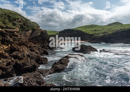Wavy sea water on rocky coast with green hills Stock Photo