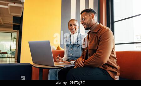 Colleagues working together in an office lobby. Two happy businesspeople smiling happily while having a discussion. Two young entrepreneurs using a la Stock Photo