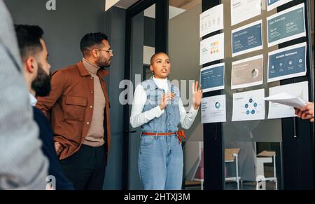Young businesswoman discussing some reports with her team. Group of multicultural businesspeople having a meeting in a modern boardroom. Diverse entre Stock Photo