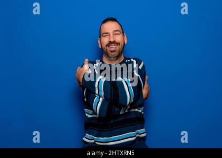 You don't need a girlfriend if you can hug yourself. Selfish feeling concept. Funny latin guy in striped sweater hugging himself and smiling with Stock Photo