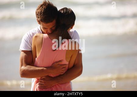 Ill never let go.... Cropped shot of a young man comforting his girlfriend while standing on the beach. Stock Photo