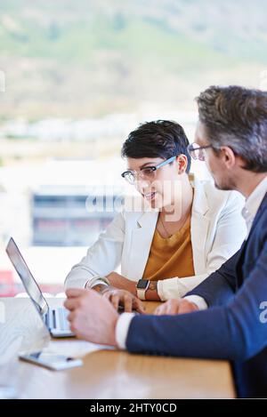 Sharing ideas for the betterment of business. Shot of two colleagues working on a laptop at a desk in an office. Stock Photo