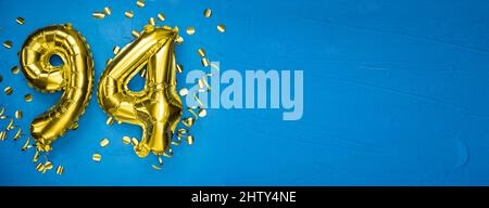 golden yellow foil balloon on blue concrete background number ninety four. Birthday or anniversary card with 94 inscription. Anniversary celebration. Stock Photo