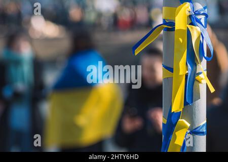 Ribbons with colors of Ukraine during a peaceful demonstration against war, Putin and Russia, with Ukrainian flag on background Stock Photo