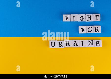 The sentence 'Fight for Ukraine' composed of letters on the background of Ukrainian flag. Photo taken under artificial, soft light Stock Photo