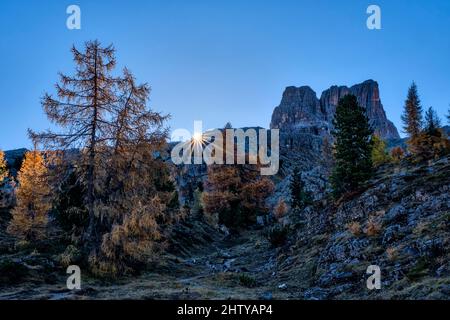 The sun is rising next to the summit of Monte Averau, seen from Lake Limedes, in autumn. Stock Photo