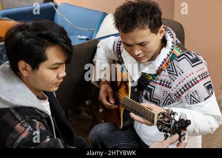 (220303) -- GUIYANG, March 3, 2022 (Xinhua) -- Bassist Peng Wanhai (L) helps guitarist Yang Zhi tune his guitar in Guiyang, southwest China's Guizhou Province, March 1, 2022. A band named 'Fish Mint' consists of three massage therapists and a delivery man who were all born in the 1990s. Yet the delivery man is the only one who could see while the rest are with visual impairment. The members do their regular work during the day and gather around to play music in the band in the evening. The band is named after fish mint, as the members think they bear a resemblance to it. Fish mint, the l Stock Photo