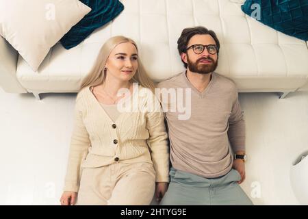 adorable caucasian blonde long-haired young woman laying down on the floor with her brunet bearded partner and looking up, contemplating future. High quality photo Stock Photo