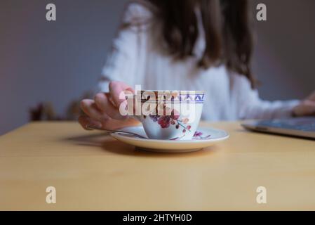 Young woman is holding a cup whilst working indoors at the desk Stock Photo