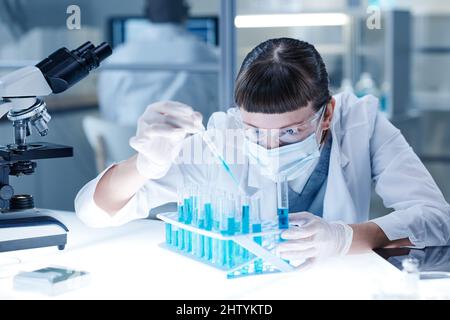 Medical or scientific researcher or doctor looking at test tube with blue liquid and using pipette to obtain the sample in a laboratory Stock Photo