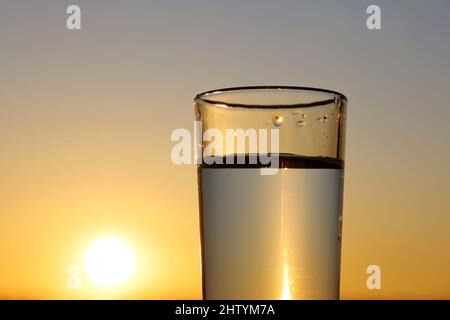 Clean water in drinking glass on sunset sky background. Concept of health and freshness, thirst, water purification Stock Photo