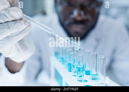 African scientist adding blue liquid with pipette into flask while examining samples in laboratory Stock Photo