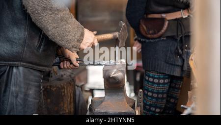 An anonymous smith, blacksmith forging a horseshoe hammering, hitting hot metal on an anvil using a hammer, hands closeup, detail, one person. Old job Stock Photo