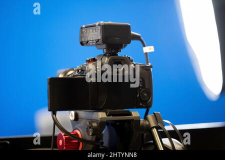 A modern professional high end mirrorless video camera on a tripod stand, bluescreen chroma key studio background, lights, live transmission recording Stock Photo