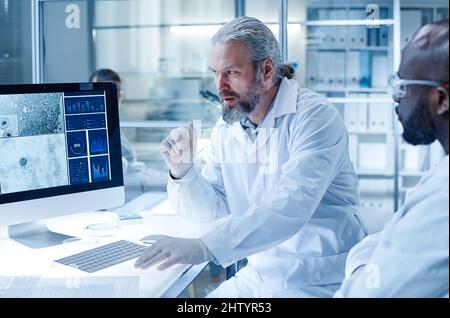Two scientists discussing the image of bacterium on computer monitor during scientific experiment in laboratory Stock Photo