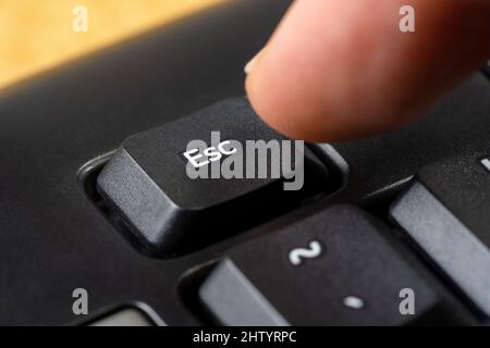 Man pressing the escape key on a simple black office keyboard, finger pushing the esc key button, object macro, extreme closeup, detail. Escaping, sto Stock Photo