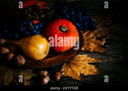 Thanksgiving composition with autumn fruit in wooden plate with maple leaves. Pumpkin and grapes vintage still life scene. November festive holiday fo Stock Photo