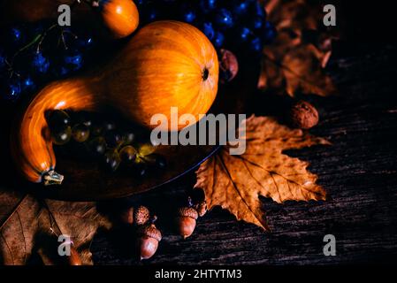 Thanksgiving composition with autumn fruit in wooden plate with maple leaves. Pumpkin and grapes vintage still life scene. November festive holiday fo Stock Photo