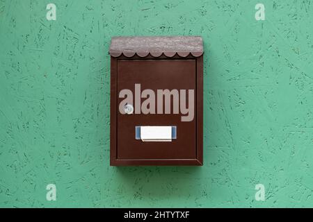 One single simple locked apartment letterbox with an empty blank name tag, classic traditional residence mailbox hanging on a green wall, metal mail l Stock Photo