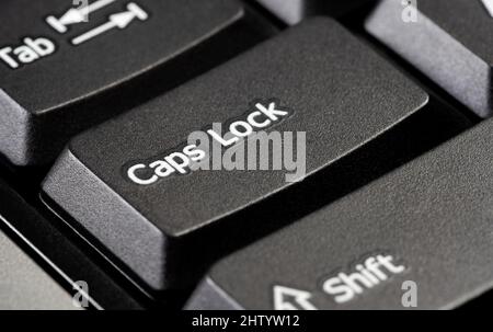 Single caps lock key on a simple black desktop PC computer keyboard, object detail, extreme closeup. Using capital letters, typing in all caps, scream Stock Photo