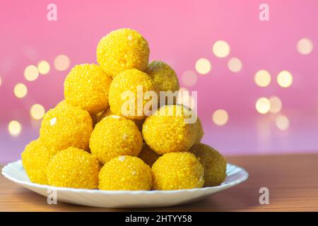 Laddu sweet stacked in white ceramic plate with pink background and yellow bokeh. Bundi Laddu made during many festivals in India specially in hindu. Stock Photo