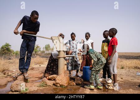 Group of black African school age children gathering around a sub saharian village faucet collecting water for their families: Recurrence of World Wat Stock Photo