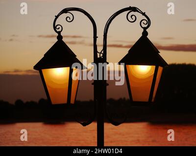 Wrought-iron lantern illuminated, as a silhouette in front of the sky illuminated by the sunset in the blurred background. Enough space on the windows Stock Photo