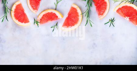Top view of pink grapefruit slices and rosemary herbs on luxury marble table. Red citrus fruit frame background. Flat lay. Stock Photo