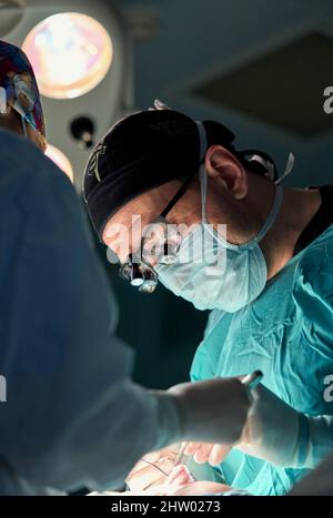 In the hospital operating room. An international team of professional surgeons and assistants works in a modern operating room. Professional doctors c Stock Photo