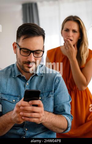 Young couple with smartphone having quarell and marriage conflict because of cheating Stock Photo