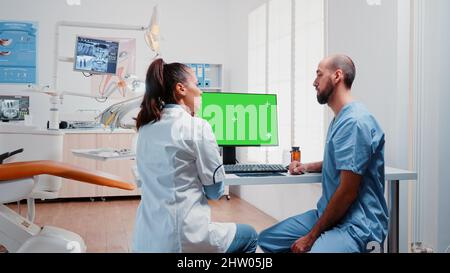 Dentistry team analyzing teeth x ray and green screen on monitor at dentist office. Specialist and man nurse working with isolated mockup template and radiography for teethcare. Stock Photo