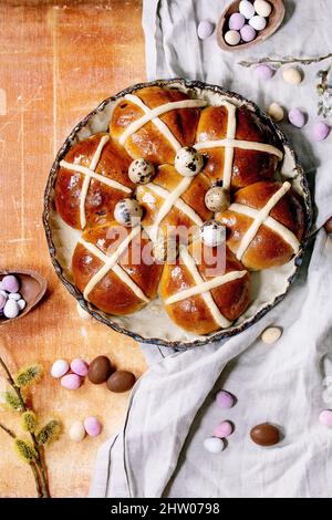 Homemade Easter traditional hot cross buns in ceramic dish with blossom willow branches and chocolate eggs colorful candies over orange stone backgrou Stock Photo