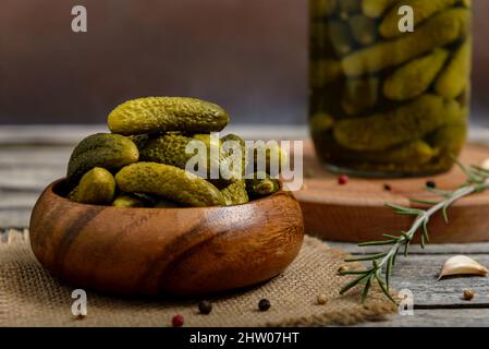 Bowl and glass jar of pickled gherkins with spices on a rustic wooden table. Selective focus. Stock Photo